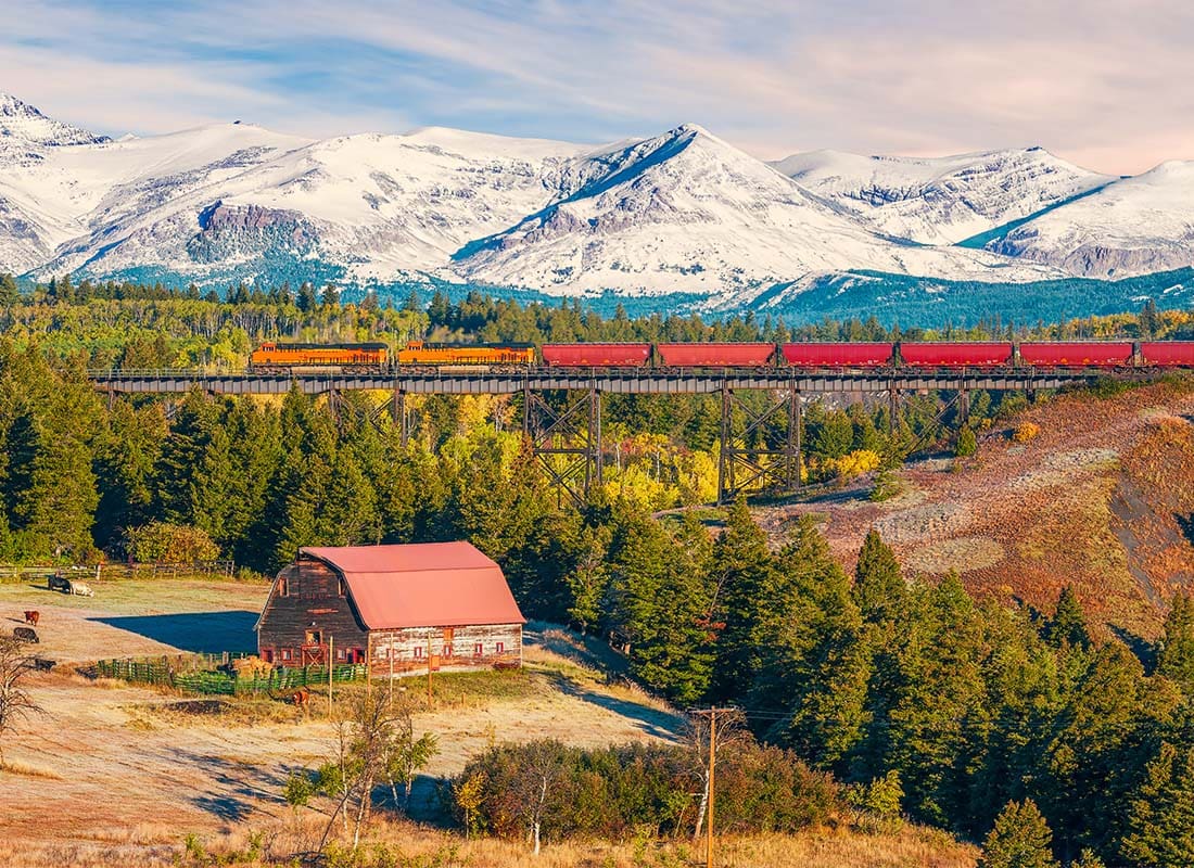 Conrad, MT - Rural Landscape of a Red Barn and Train in the Background Against the Mountains in Conrad Montana